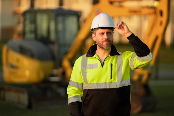 建在挖掘机上 建筑工人与挖掘机 戴头盔的建设者戴着硬礼帽的工人 戴着建筑用头盔的肖像画机械工人 工程师 建筑工人 工头或修理工 — 图库照片
