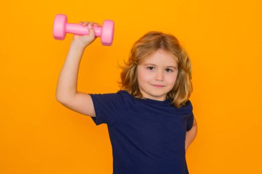 Dambılı spor çocuk portresi, sarı stüdyo arka planında izole edilmiş. Dambıllarla çalışan çocuk portresi. Çocuklar için motivasyon ve spor kavramı