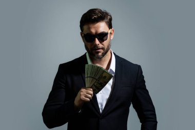 Üzerinde nakit para banknotları olan tişörtlü bir iş adamı sarı stüdyo geçmişinden izole edilmiş. 100 dolarlık banknot, finansal konsept.