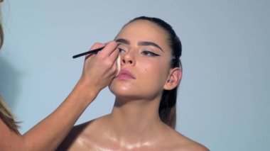 Makyaj sanatçısı kozmetik kullanıyor. Güzellik abidesi. Makyaj ustasının eli, genç güzel kızın dudaklarını boyuyor. Makyaj yapılıyor. Makyaj sanatçısı tarafından makyaj yapan güzel Asyalı bir kadın.