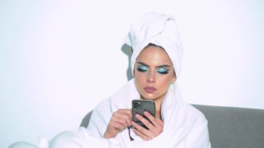 Elinde cep telefonu tutan seksi genç bir kadın. Kafasında havlu ve bornozuyla akıllı telefon tutan seksi bir kadın.