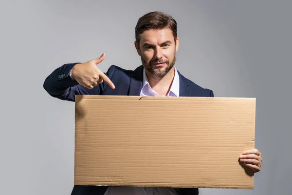 Business man holds sign, blank card. Placard ready for your product. Man in suit showing blank sign board over studio isolated background, pointing finger. Empty blank board. Area for advertising