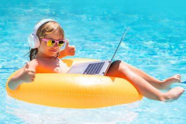 Yazın yüzme havuzunda dizüstü bilgisayarı olan bir çocuk. Yaz seyahati ve iş kavramı