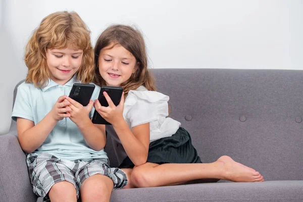 Children alone with phone at home. Sibling kids using smartphone together. Children playing game on mobile phone, watching online content on internet. Gadget addiction. Mobile addict concept