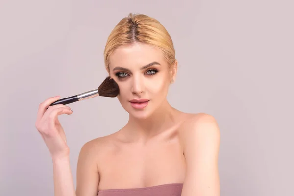 Young woman applies powder on the face using makeup brush. Beautiful girl doing contouring apply blush on cheeks. Face beauty cosmetics. Fresh skin and natural make up. Powder blush on facial skin