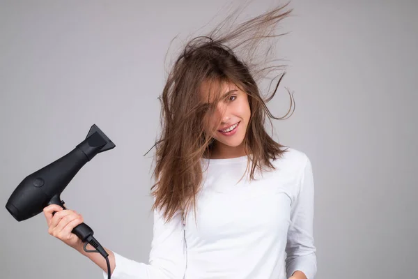 Young woman drying her hair with a hairdryer isolated on studio background. Young woman with blow dryer drying hair, making hairdo. Close up portrait of beautiful young woman in drying hairstyle