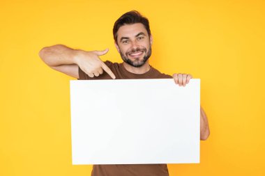 Boş afişi olan mutlu adam stüdyo arka planında izole edilmiş. Boş posteri olan çekici bir adamın portresi. Poster gösteren, tabela üzerinde parmak gösteren bir adam. Pano veya afiş konsepti