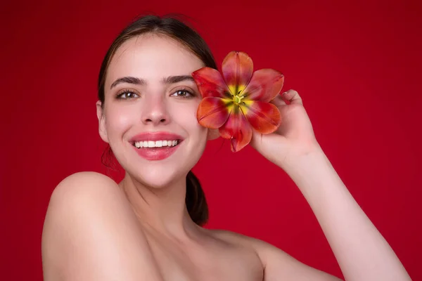 Youth and skin care concept. Beauty girl with tulip near face. Beautiful sensual woman hold tulips, studio portrait on red background