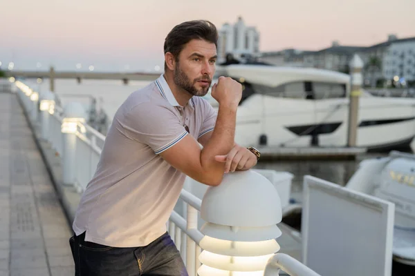 Rich business man dreaming and thinking near the yacht. Handsome man outdoors portrait. Portrait of stylish male model outdoor. Fashionable man in urban style