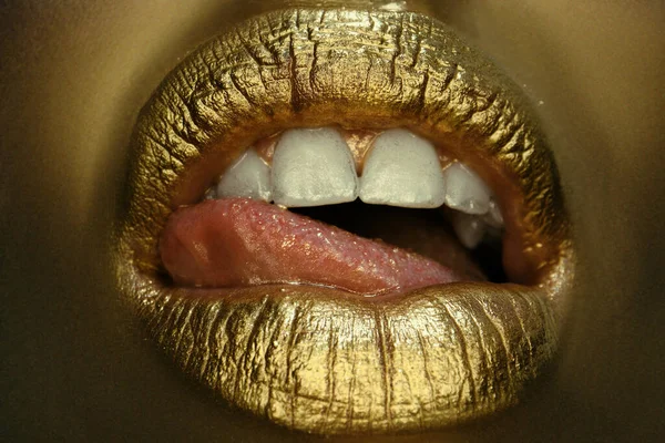 Gold lips. Gold paint from the mouth. Golden lips on woman mouth with make-up. Sensual and creative design for golden metallic. Gold concept