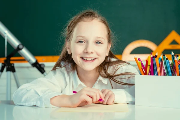 可爱的小男孩画了一栋房子 看着相机 可爱的孩子用五彩缤纷的蜡笔画 微笑着 — 图库照片