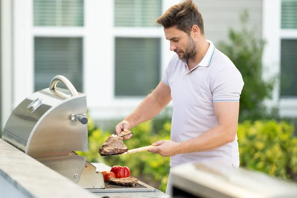 男は家の裏庭でバーベキューで肉を調理します バーベキューの準備をしてるハンサムな男 バーベキューシェフマスター おいしいグリルバーベキュー食品 バーベキュー肉を調理します グリルとバーベキュー — ストック写真