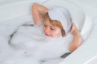 Çocuk şampuanı. Çocuk kafasında köpük. Şampuan köpüğü ve banyo yapan saçlarında kabarcıklar olan bir çocuk. Köpüklü çocuk suratı, saç bakımı ve hijyen konsepti. Çocuklar uzun saçlar için şampuan kullanırlar. Banyoda saç yıkamak.