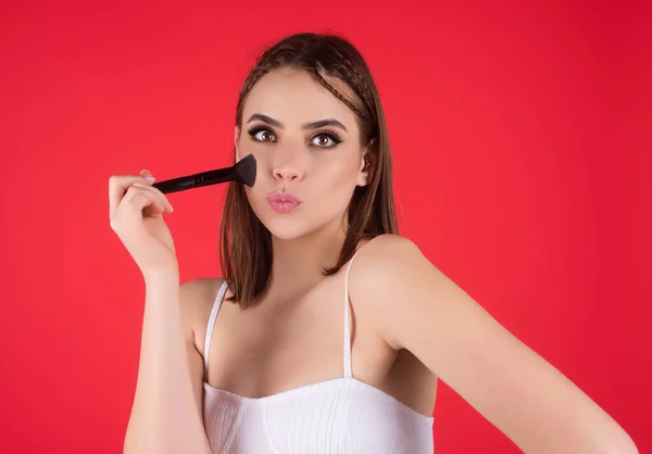 Beautiful woman applying makeup holding brush. Beauty make up concept of an young woman. Beauty salon. Skin care and natural makeup. Girl gets blush on the cheekbones. Beauty care and treatment