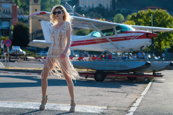 stock image Fashion young woman in stylish dress walking near jet. Woman tourist getting out of jet airplane. Summer destination travel. Summer vacation on Como lake Italy. Travel and active lifestyle concept