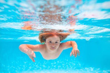 Yaz günü havuzda bir çocuk. Çocuk denizde suyun altında yüzer. Çocuk su altında havuzda yüzüyor. Mutlu çocuk suyun altında yüzüyor, aktif çocuk yüzüyor, oynuyor ve dalıyor, çocuklar su sporu yapıyor.