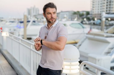 Güneş gözlüğü ve gömlek takan şık bir adam. Dışarıdaki yakışıklı adam portresi. Açık havada şık bir erkek modelin portresi. Moda erkeği sokakta gökdelenin yakınında poz veriyor. Şehir tarzı modaya uygun bir adam.