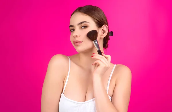 Woman applies powder on the face using makeup brush. Girl doing contouring apply blush on cheeks. Face beauty cosmetics. Fresh skin and natural make up. Powder blush on facial skin