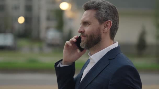 携帯電話を使用して外の正式なスーツを着たビジネスマン ビジネスマンは通りを歩いて電話をしている 大人の男が電話で話してる 電話を使った正式な訴訟のビジネスマン — ストック動画