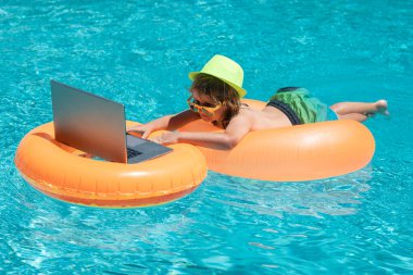 Kumsalda çalışmak ve dinlenmek. Çocuk yüzme havuzunda dizüstü bilgisayarla çalışıyor. Yaz işleri.