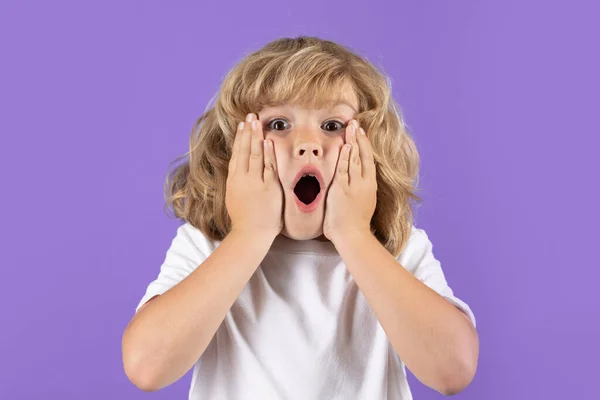 Shocked kid boy keeping hands near cheek with open mouth on studio isolated background. Surprised face, excited emotions of child. Shock, omg and wow expression