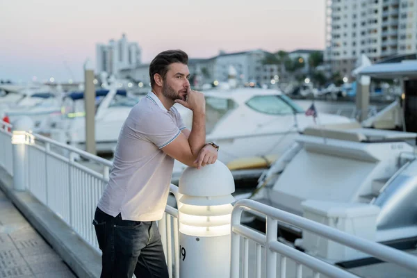 Rich businessman dreaming and thinking near the yacht. Handsome confident stylish hipster model posing outside. Sexy fashion male in the street background in American city