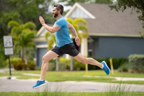 Man running on street in neighborhood. Handsome athlete running in the street. Full length shot of man in sportswear running, urban training