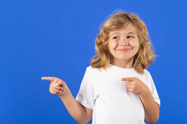 Child boy pointing away on blue isolated studio background. Portrait of cute smiling child, isolated studio background. Happy kid, happy and smiling emotions