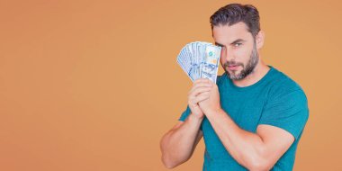 Bej renkli stüdyo pankartına para yatıran adam. Dolar banknotları olan takım elbiseli zengin bir adam. Dolar banknotlarıyla başarılı bir iş adamı