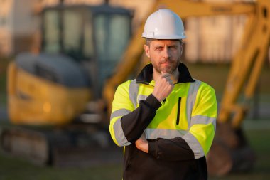 Kazıcının yanındaki inşaatçı. Kazıcılı inşaat işçisi. Miğferli miğfer. Şapkalı bir işçi. İnşaat miğferinde portre mekaniği işçisi. Mühendis ustabaşı veya tamirci.