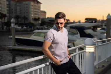 Güneş gözlüğü ve gömlek takan şık bir adam. Dışarıdaki yakışıklı adam portresi. Açık havada şık bir erkek modelin portresi. Moda erkeği sokakta gökdelenin yakınında poz veriyor. Şehir tarzı modaya uygun bir adam.