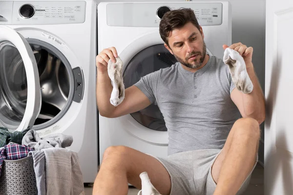 Çamaşır makinesinin önünde kirli çamaşırları olan adam.