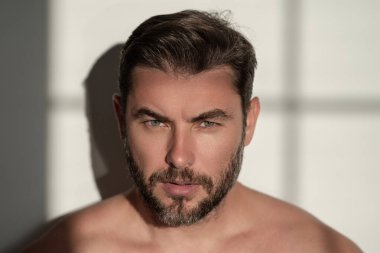 Kırklı yaşlarda yarı çıplak bir adamın portresi beyaz arka planda izole edilmiş. Yakışıklı, ciddi bir adam, taze, pürüzsüz bir cilde sahip. Mükemmel yüzlü güzel bir adamın portresi.