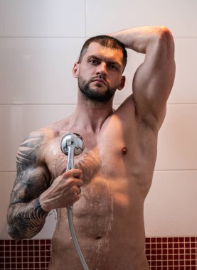 Sexy muscular man taking shower washing his body, back and shoulders. Handsome guy standing in the bathroom under hot water drops. Hygienic cleansing routine in bathroom. Skincare and bodycare