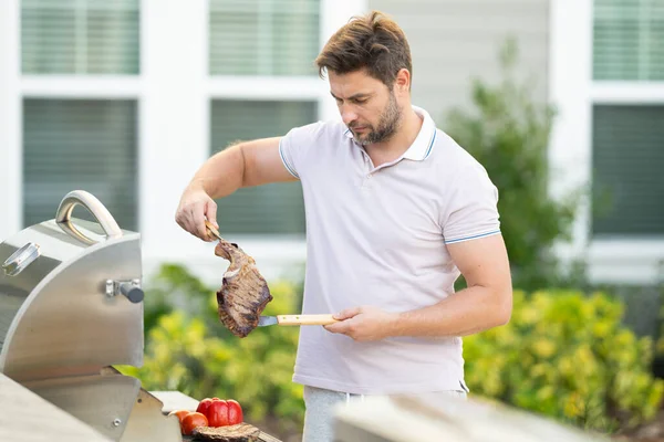 男性シェフは庭でグリルし バーベキューをします バーベキュー屋外ガーデンパーティー バーベキューの肉を準備するハンサムな男 夏の間の屋外での食事と料理の概念 — ストック写真