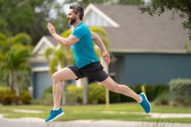 Koşan adam dışarıda koşuyor. Amerikan mahallesinde koşan formda bir sporcu. Beyaz tenli erkek, spor mankeni dışarıda uzun süre çalışıyor.