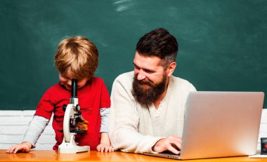 İlkokul öğretmeni ve sınıf öğrencisi. Baba okul çocuğuyla oynuyor. Öğretmen ve öğrenci sınıfta dizüstü bilgisayar kullanıyor. Öğretmenler, sınıftaki öğrencilerin ders çalışmasına yardım ediyor.