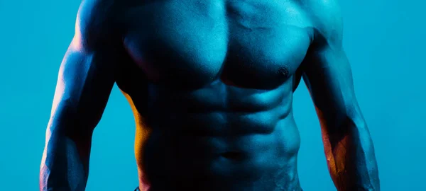Muscular model sports young man on blue dark background. Fashion portrait of strong brutal guy with a modern trendy blue color. Sexy bare torso. Sport workout bodybuilding concep