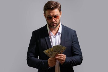 İyi ödeme. Yakışıklı adam gri stüdyoda izole edilmiş para tutuyor. Dolar banknotları halinde para. Yığınla para, finans, yatırım ve tasarruf. Model pankartı
