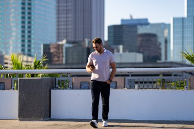 Şehir merkezinde sıradan, yakışıklı bir manken. İyi giyimli, gözlüklü ve polo pozu veren bir adam. Erkek model. Şehirde şık bir adamın portresi. Açık hava moda portresi