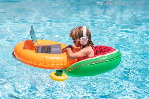 Freelance work, distance online work, e-learning. Summer business. Kid remote working on laptop in pool. Little business man working online on laptop in summer swimming pool water