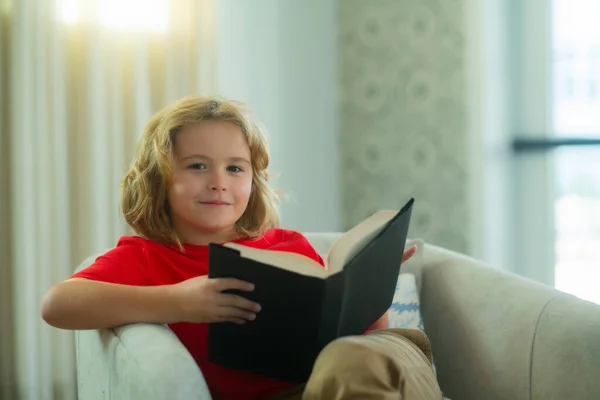 Child reading book at living room. Kids read books. Little boy sitting on couch in sunny living room watching pictures in story book. Concept of education, childhood, book reading and inspiration