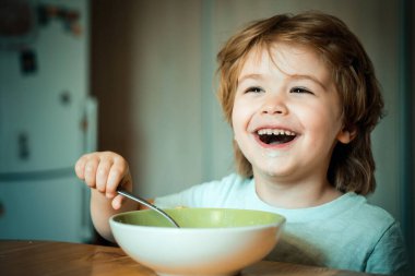 Çocuk yiyor. Küçük çocuk mutfakta kahvaltı yapıyor. Mutfakta meyve püre yiyen mutlu sevimli bebek gülümseyen. Aç küçük çocuk yeme
