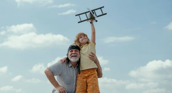 Grandfather and son with toy plane over blue sky and clouds background. Men generation grandfather and grandson playing outdoors