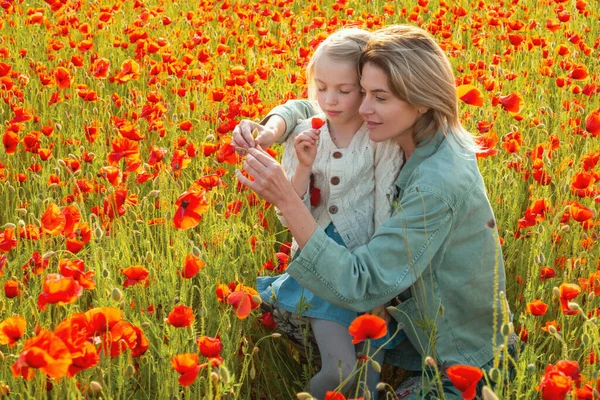 Happy spring family. Beautiful child girl with young mother are wearing casual clothes in field of poppy flowers. Family on spring poppy field