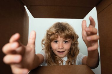 Çocuk karton kutuyu açar ve içinden hediyesini çıkarır. Küçük çocuk paket kutusuna bakıyor ve bir sürpriz aldığına seviniyor. Yüzünde neşe beliren genç bir çocuk. Çocuklar için kutu ve teslimat paketini aç