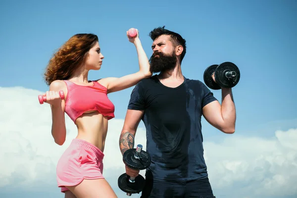 Athletic couple of fit man and woman with a dumbells outdoors. Couple doing fitness outside. Young fitness couple