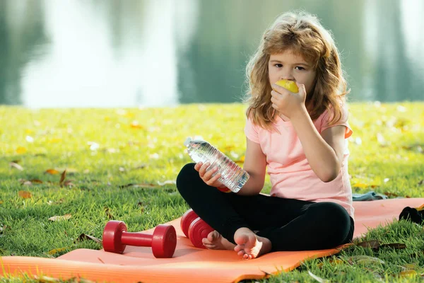 Sport kids boy. Child boy eat apple rest on sport mat after sport exercises outdoor in park