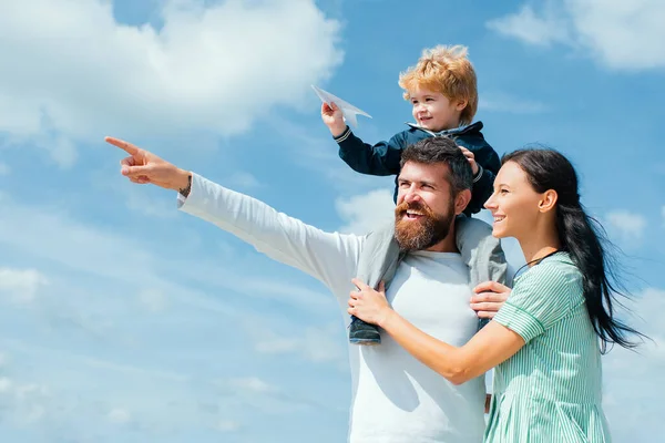 Daddy, mommy and child son. Happy family - child son playing with paper airplane. Portrait of happy father giving son piggyback ride on his shoulders, hug wife and looking up