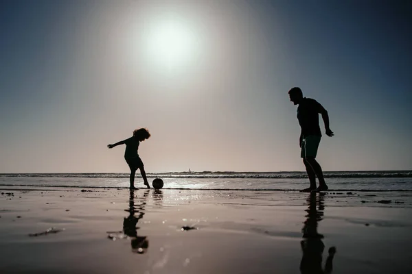 父と息子はビーチでサッカーやサッカーをしたり 日没のシルエットをしたりします 屋外で楽しむお父さんと子供 ライフスタイルと家族の休暇 幸福の男性の概念 — ストック写真